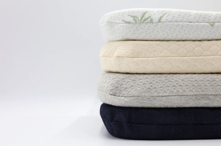Stack of 100% organic latex seat cushion with organic cotton, denim, and bamboo covers in various colors on a light blue background